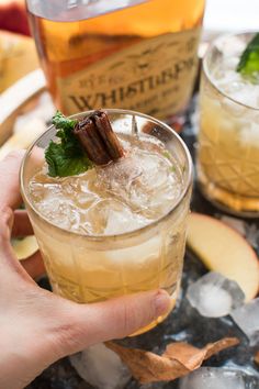 a person holding a drink in front of an apple cider and ice cubes