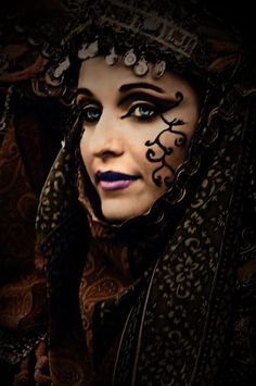 a woman with blue eyes wearing a black and brown mask on her face, covered in lace