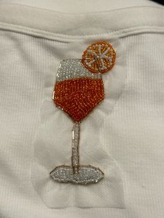 a white shirt with an orange and wine glass embroidered on the front, along with silver sequins