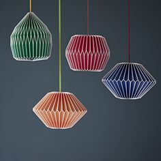 three different colored paper lamps hanging from strings on a gray background, one is red, one is blue and the other is green