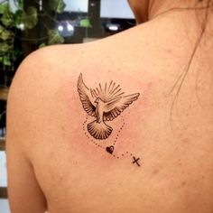 the back of a woman's shoulder with a dove and cross tattoo on it