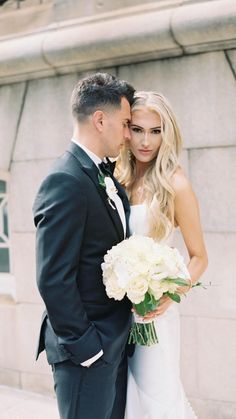 a bride and groom standing next to each other in front of a stone wall with white flowers