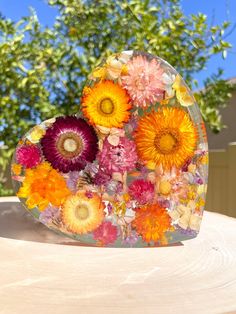 a heart shaped vase filled with flowers on top of a wooden table next to a tree