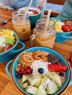 three bowls filled with different types of food on top of a wooden table in front of two people