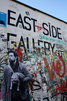 a man holding a cat in front of a wall covered with graffiti