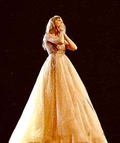 a woman in a gold dress standing on a stage with her hands to her face