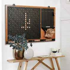 a wall mounted scrabble board with vases and books on it next to a wooden table