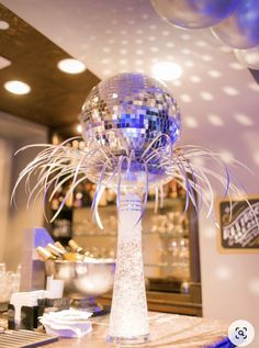 a disco ball is on top of a tall glass vase with some silver foil around it