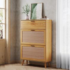 a wooden cabinet with two drawers in front of a window next to a painting on the wall