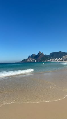 a beach with waves coming in to the shore and some mountains in the back ground