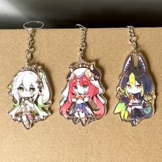 three keychains with anime characters on them sitting on a brown surface next to each other