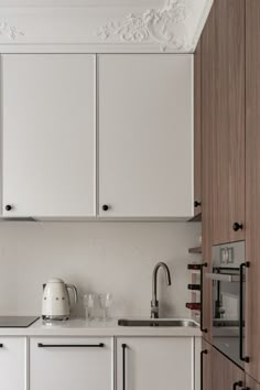 a kitchen with white cupboards and an oven in the corner, along with a coffee pot on the counter