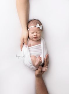 a newborn baby wrapped in a white wrap being held by someone's arm and holding it