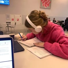 a girl is writing on her notebook while listening to headphones