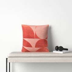 an orange and pink pillow sitting on top of a white bench next to a pair of headphones