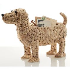 a woven dog figurine holding money in it's mouth and standing on a white surface