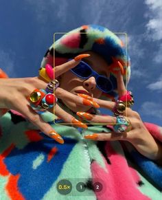 a woman with colorful nails and sunglasses holding up her hand in front of the camera