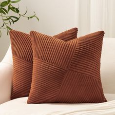 two brown pillows sitting on top of a white couch next to a potted plant