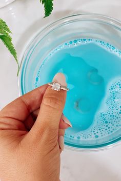 a woman's hand holding an engagement ring in front of a blue drink with mint sprigs