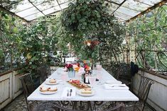 an outdoor dining area with tables and chairs covered in greenery, surrounded by potted plants