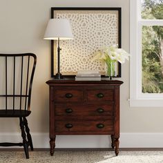 a wooden dresser sitting next to a chair with a lamp on top of it near a window