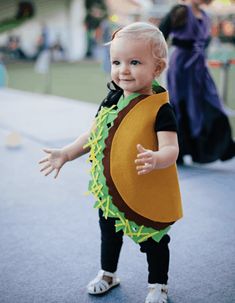 a baby dressed in a costume is standing on the ground with his hands out and smiling