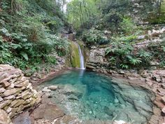 there is a small waterfall in the middle of this pool with blue water and rocks