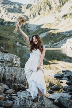 a woman in white dress standing on rocks with her arms outstretched and flowers in the air