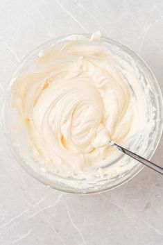 a bowl filled with cream sitting on top of a white counter next to a spoon