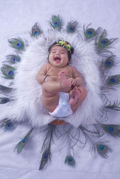 a baby is laying down with feathers on it's back and its mouth open