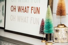 three christmas trees are sitting on a mantle next to a sign that says oh what fun oh what fun