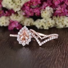 a pink diamond ring sitting on top of a wooden table next to purple and white flowers