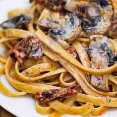 a white plate topped with pasta covered in mushrooms and sauce on top of a wooden table