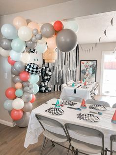 a room filled with balloons and tables covered in white table cloths, black and white checkered napkins