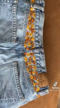 the back pocket of a pair of jeans with yellow flowers on them and an orange ribbon