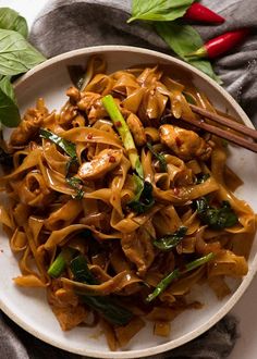 a white bowl filled with noodles and vegetables on top of a table next to chopsticks