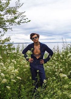 a man standing in tall grass with his hands on his hips wearing sunglasses and looking at the camera