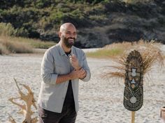 a man standing in front of a wooden mask on the beach next to some grass