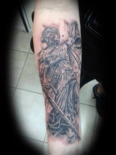 a man's arm with a statue and cross tattoo on the left side of his arm