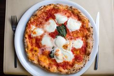 a small pizza with cheese and spinach on a white plate next to silverware