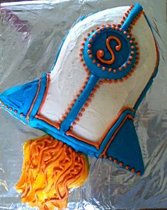 a cake shaped like a rocket ship on top of tin foil with orange and blue icing