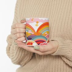 a woman holding a coffee mug in her right hand, with an image of a rainbow on it