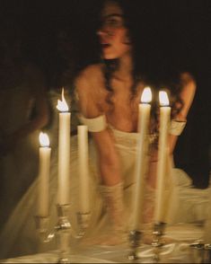 a woman sitting in front of candles with her face obscured by the candle holder behind her