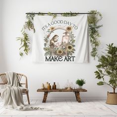 a white wall hanging over a wooden table next to a chair and potted plant