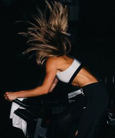 a woman riding on the back of a bike in front of a dark background with her hair blowing