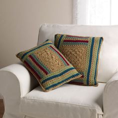 two crocheted pillows sitting on top of a white couch