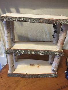 three tiered shelf made out of birch logs on top of a wooden table next to a blue vase