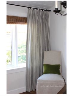 a white chair sitting in front of a window with a green pillow on top of it