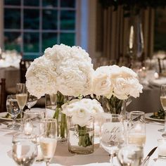 white flowers are in vases on a table with wine glasses and silverware around it