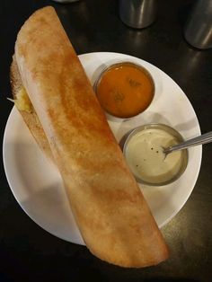 a long sandwich on a plate with dipping sauces